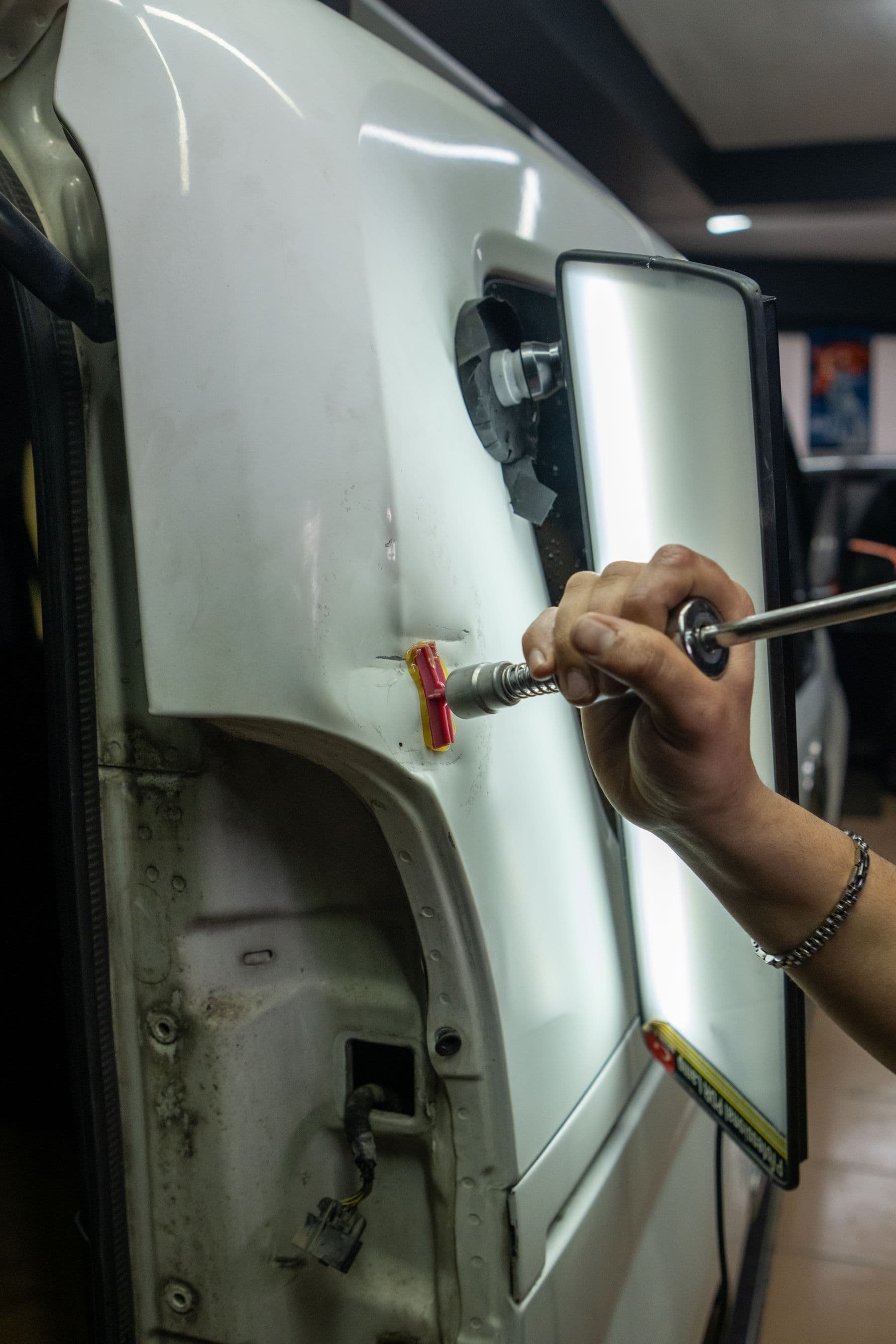 Technician pulling a dent out of a white car door with a slide hammer