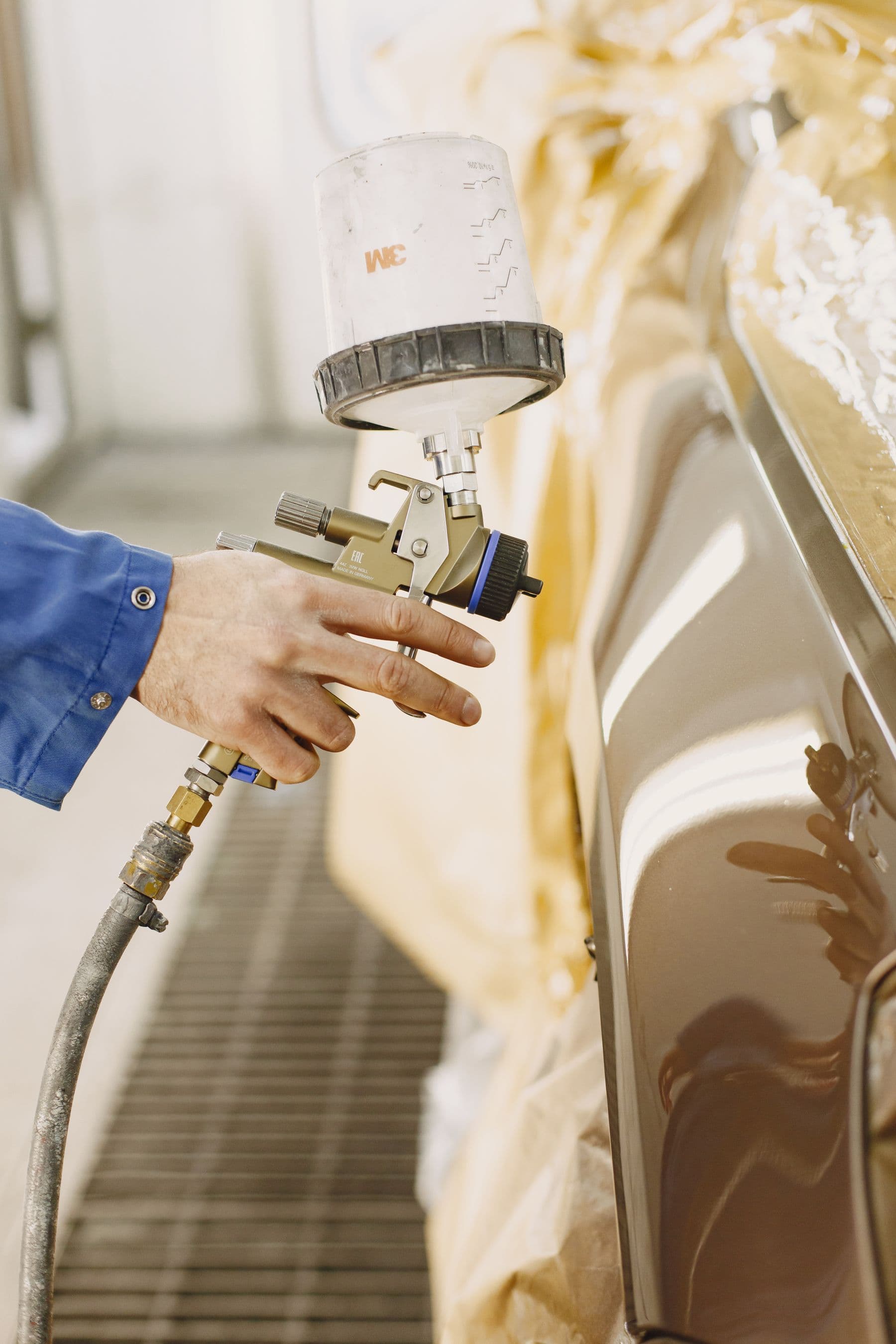 Spray gun laying colour on a masked car panel inside a paint booth