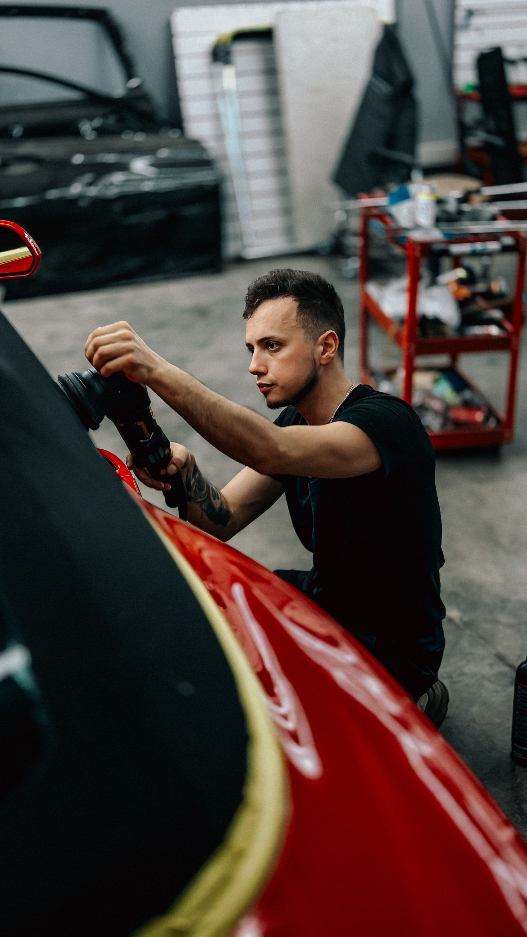 Technician machine-polishing the panel of a red car in the shop